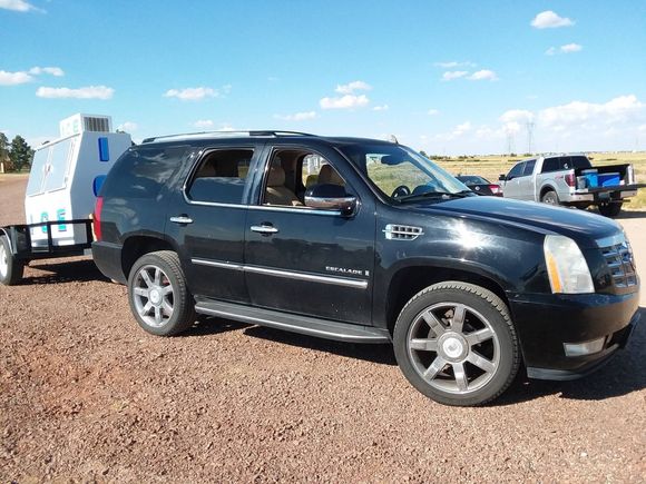 Black SUV towing a light blue trailer on a dirt road under a blue sky.