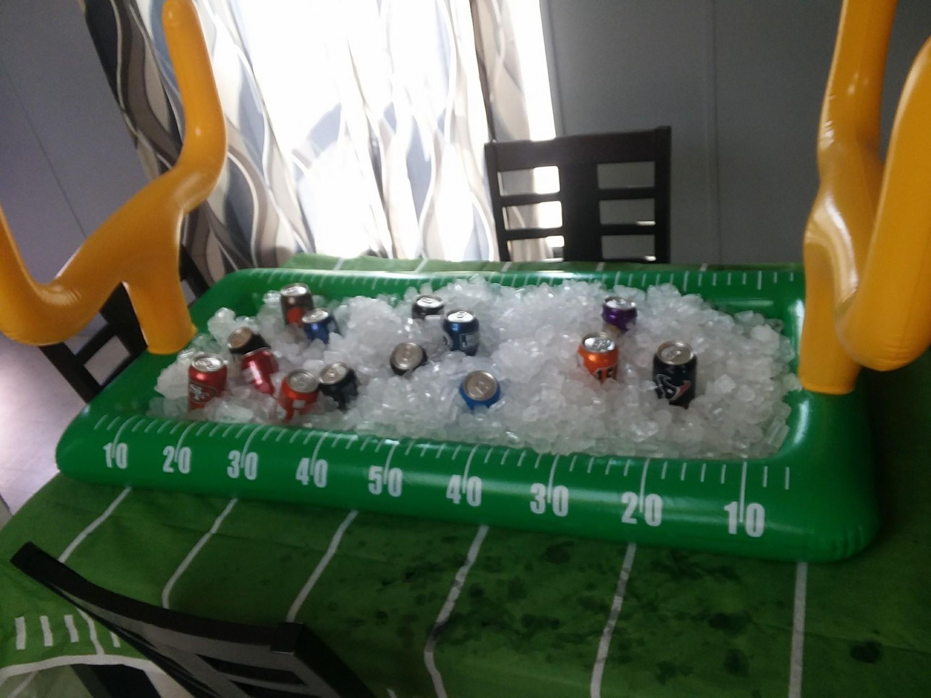 Inflatable football field cooler filled with ice and cans, on a green cloth, with yellow goalposts.