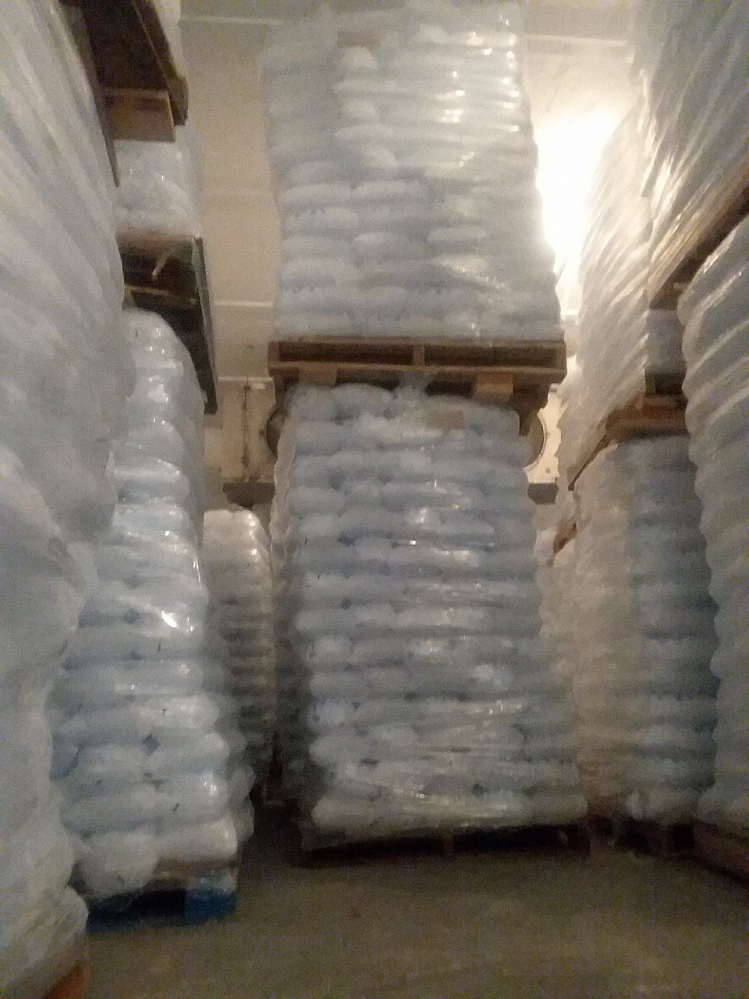 Stacks of white bags on pallets in a warehouse. Wrapped in clear plastic, reaching ceiling.