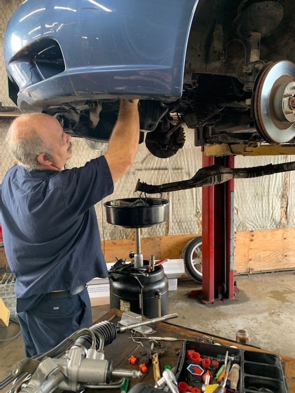A mechanic works on the undercarriage of a raised blue car in a repair shop with an oil drain pan positioned below.