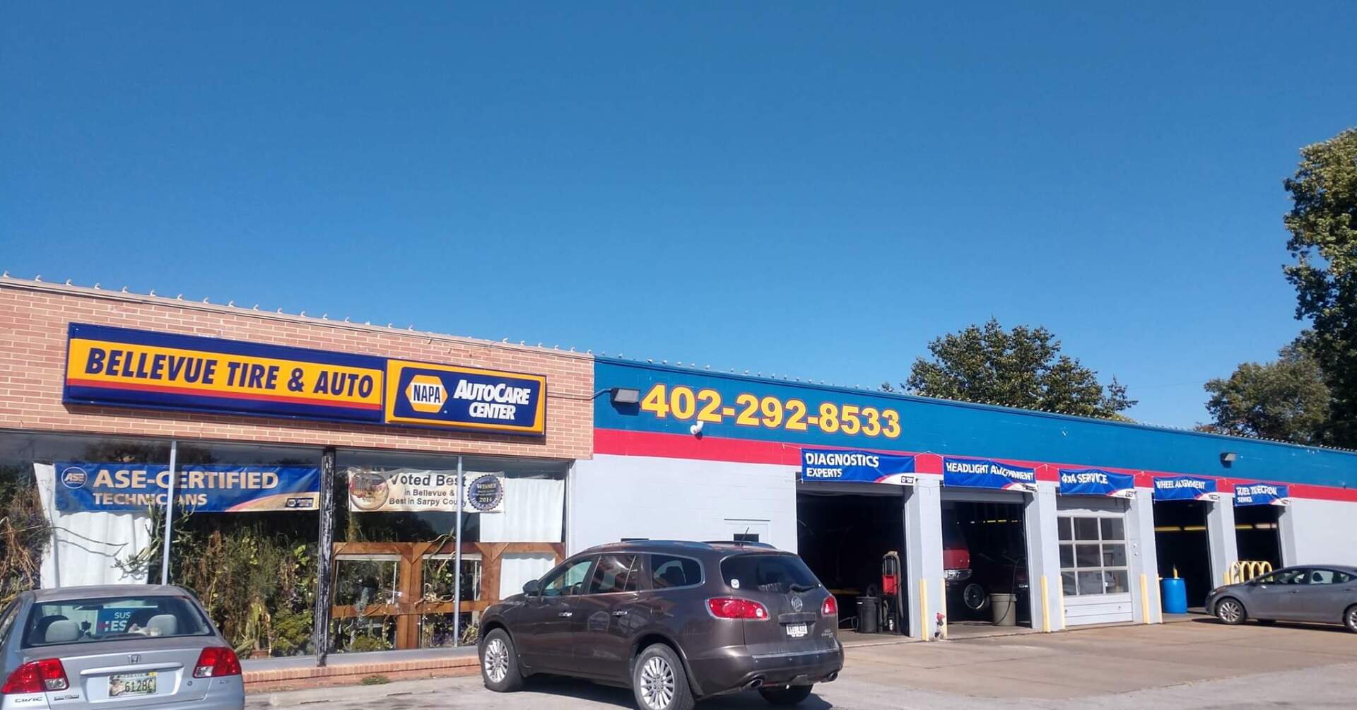 Auto repair shop exterior with blue awning, yellow signage, and cars parked out front