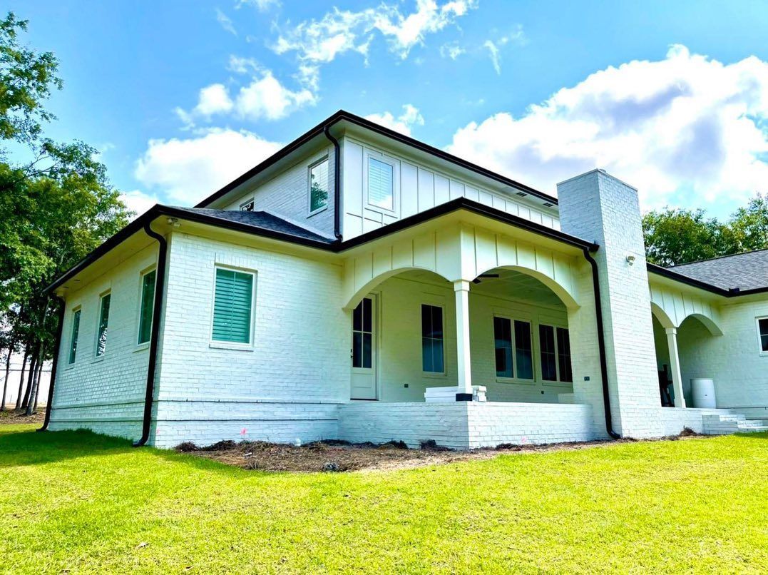 White house with black trim, a covered porch, and a tall chimney under a blue sky.