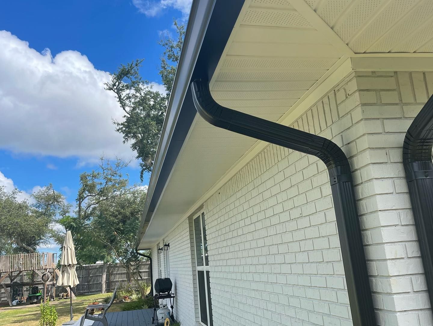 Black gutter system on a white brick building under a partly cloudy sky.