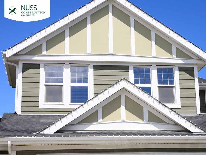 The upper exterior of a house featuring sage green siding with white trim and two stacked, gabled roof sections.