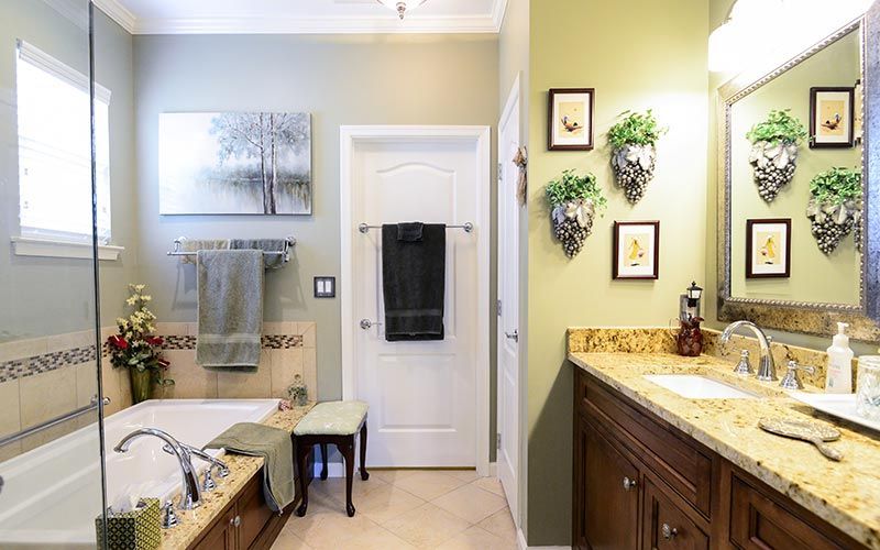 A bathroom with a soaking tub, a brown wood vanity with granite counters, and light green walls decorated with wall art.