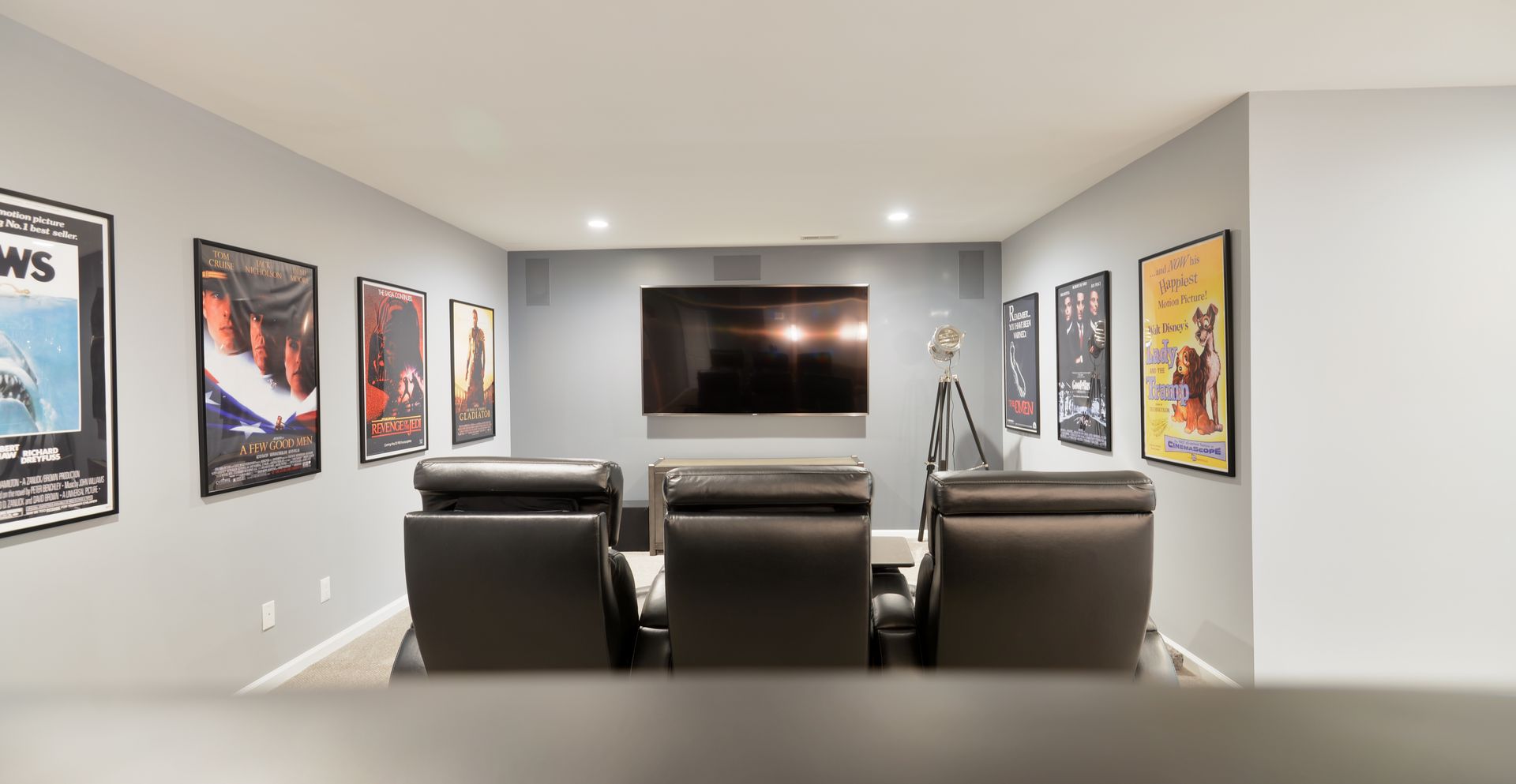 A home theater with three leather recliners facing a wall-mounted television, decorated with framed movie posters.