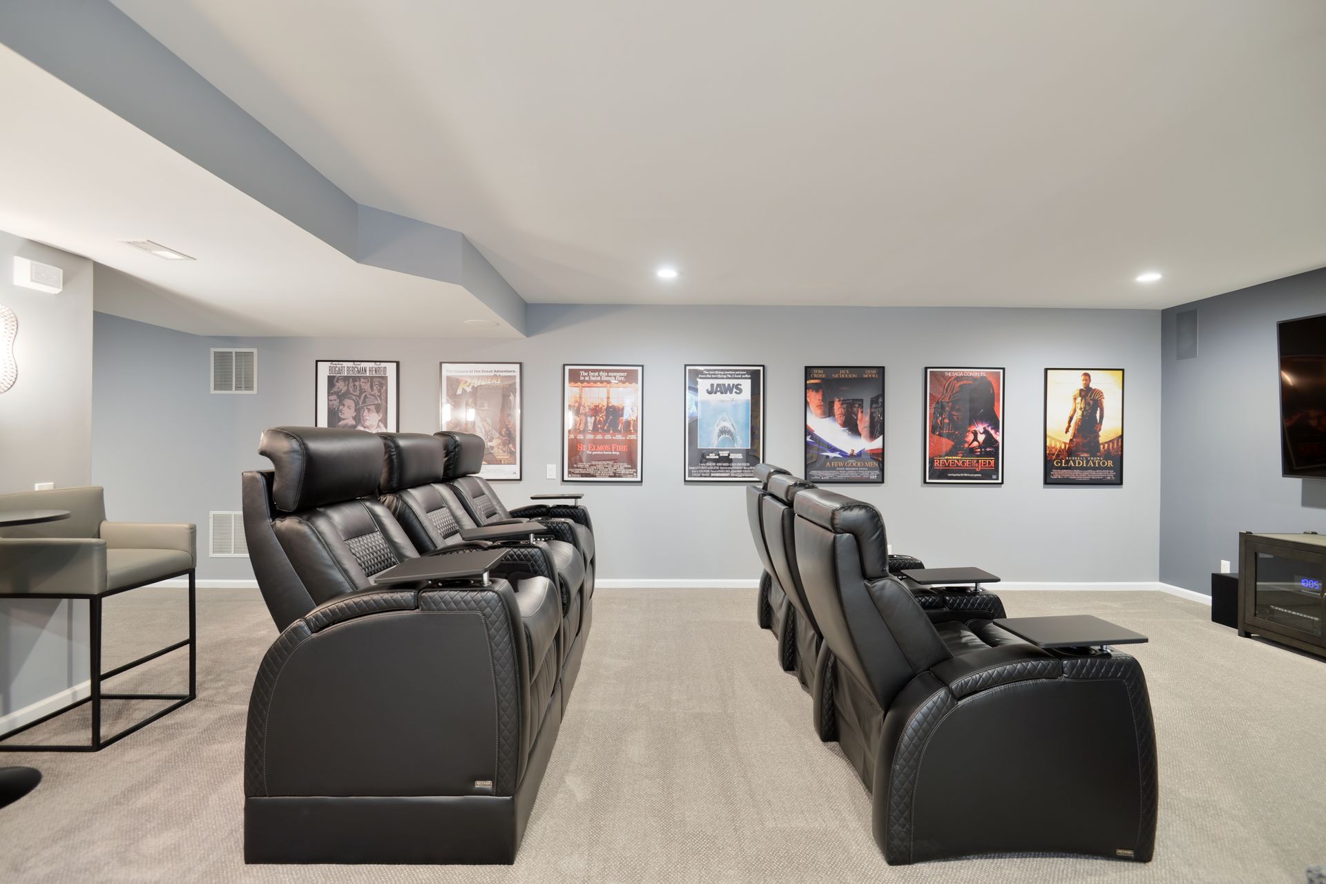 A home theater featuring two rows of black leather reclining seats, gray walls, and framed movie posters.