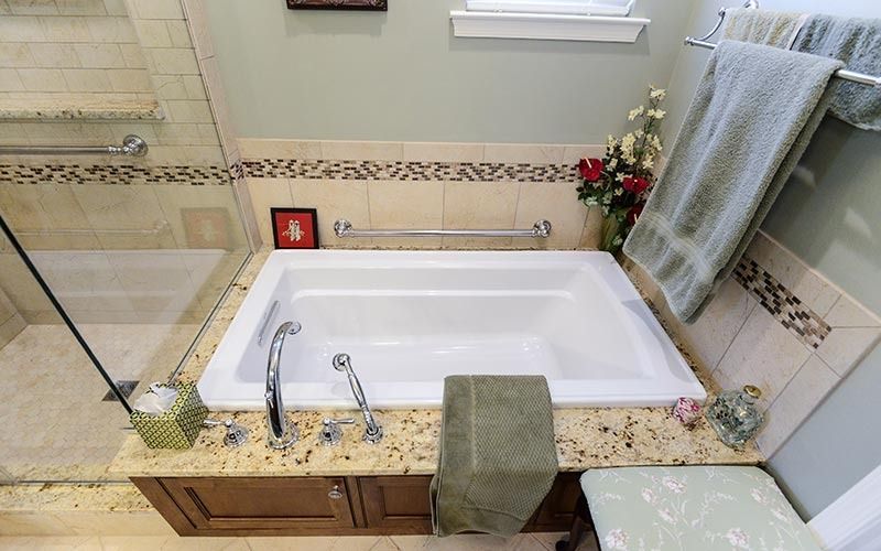 A white soaking tub with granite surround and chrome fixtures, positioned next to a glass-enclosed shower in a bathroom.
