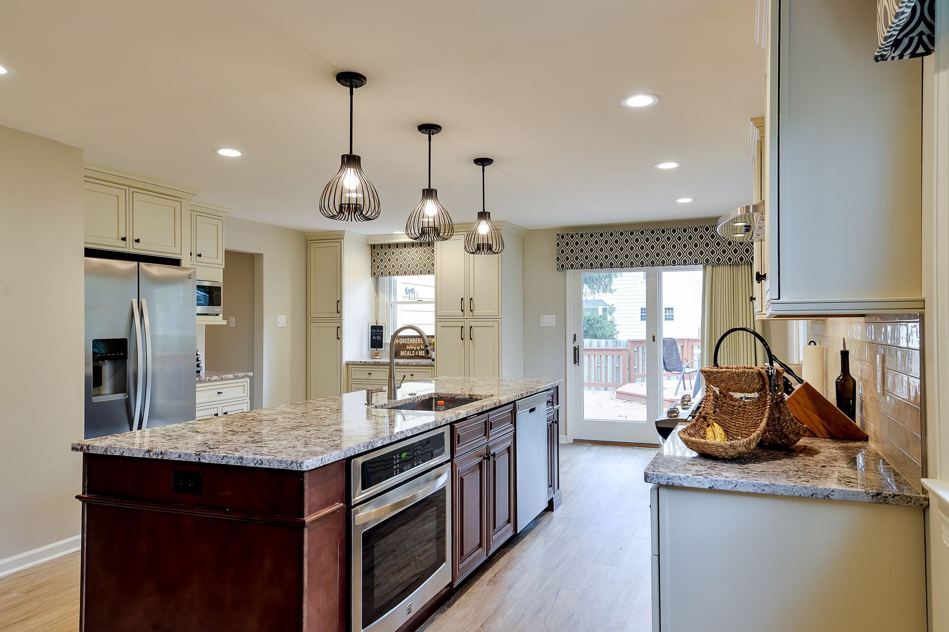 A modern kitchen featuring a dark wood island with a granite countertop, pendant lights, and stainless appliances.