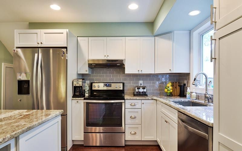 Modern kitchen with white cabinets, stainless steel appliances, granite countertops, and light green walls.