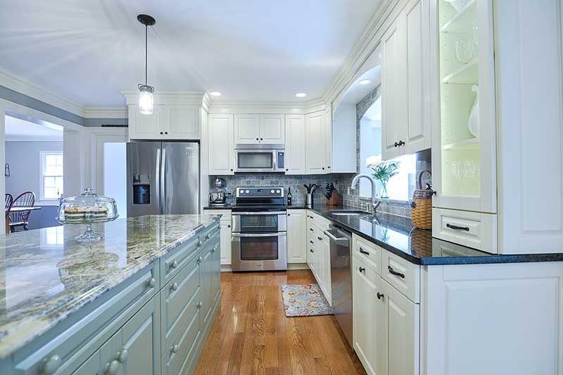 A bright, modern kitchen featuring white cabinets, sage green island base, stainless steel appliances, and wood floors.