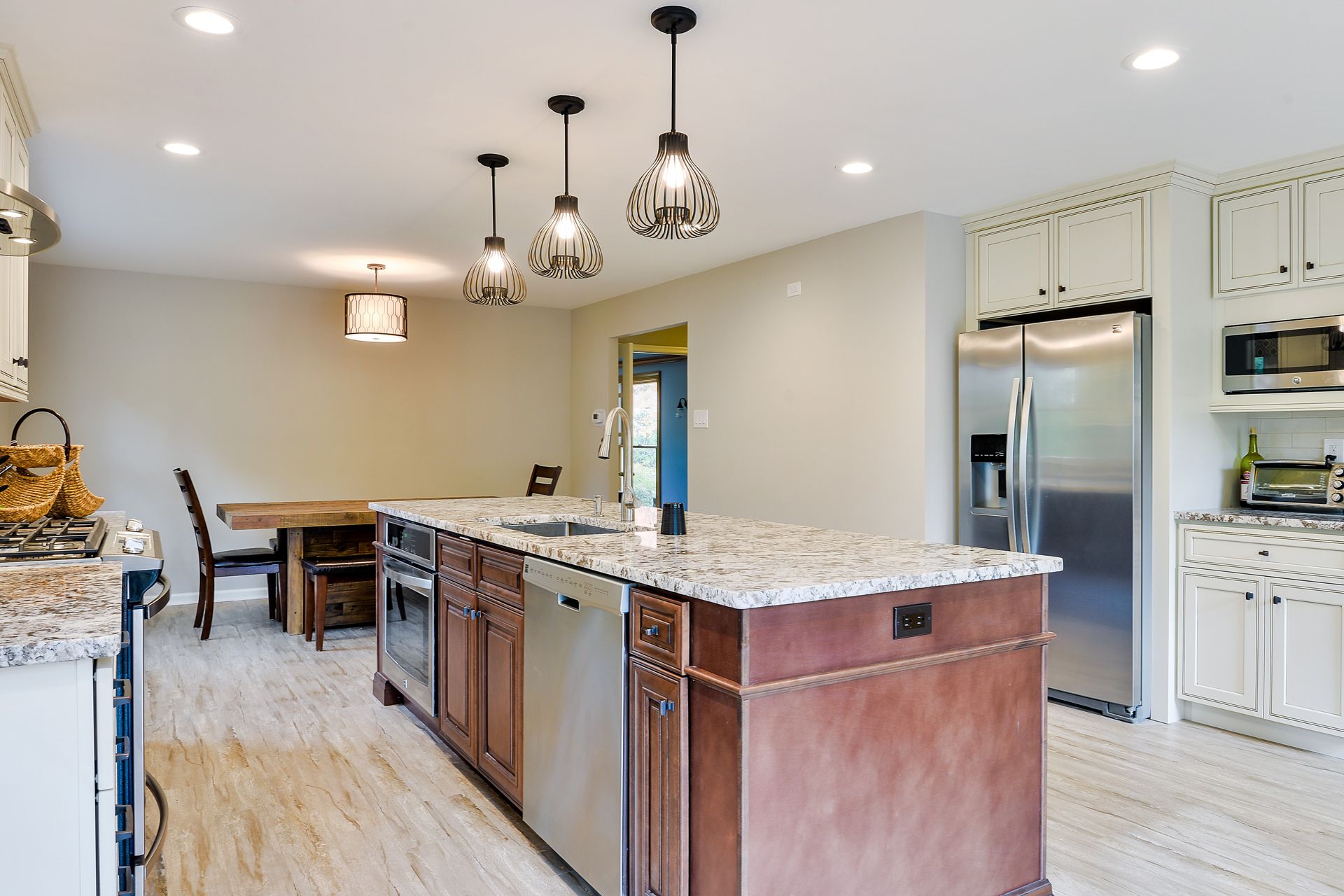 A bright kitchen with a large granite-topped island, wooden cabinets, stainless steel appliances, and a dining area.
