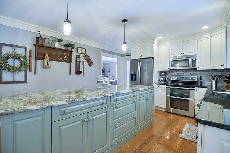 A kitchen featuring a light green island with a granite countertop, white cabinets, stainless appliances, and wood floors.