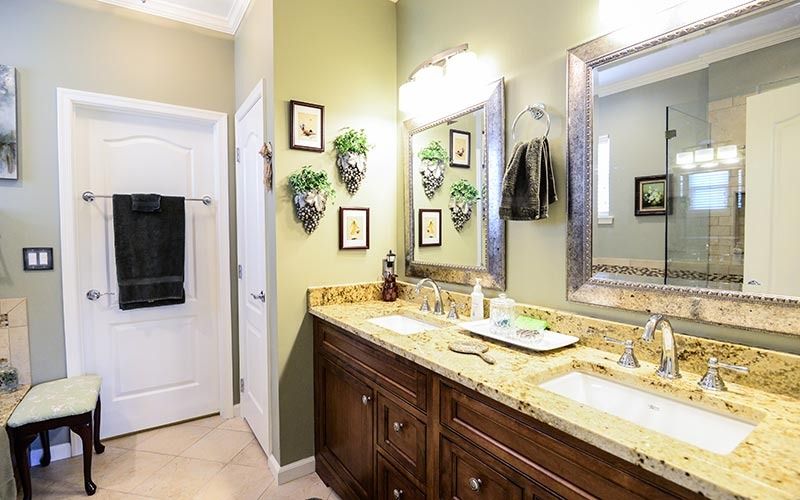 A bathroom with sage green walls, a dark wood vanity with granite counters, dual mirrors, and a white door with a towel.