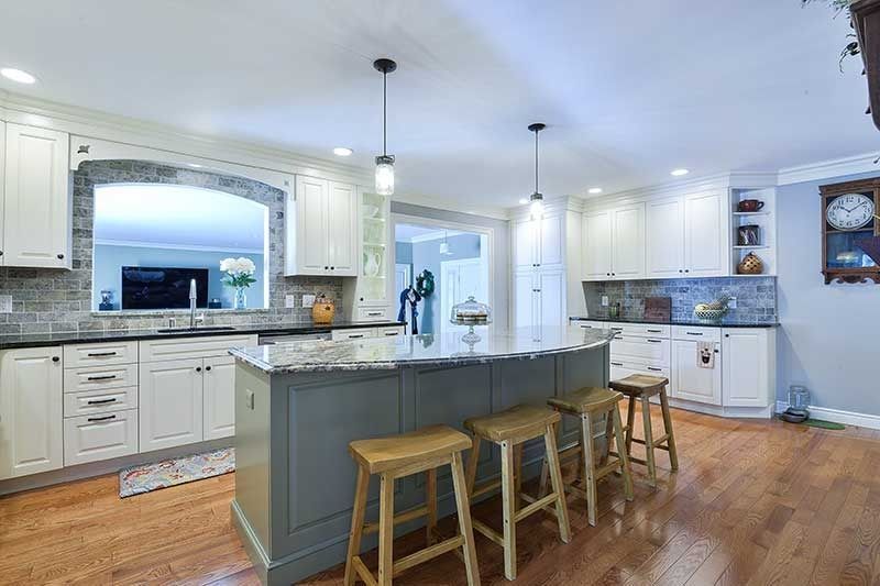 A bright kitchen with white cabinets, a gray central island with wooden stools, and hardwood floors.
