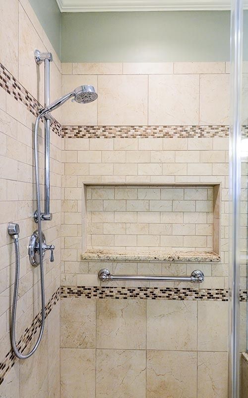 A walk-in shower with beige subway tiles, a recessed storage niche, a metal grab bar, and an adjustable shower head.