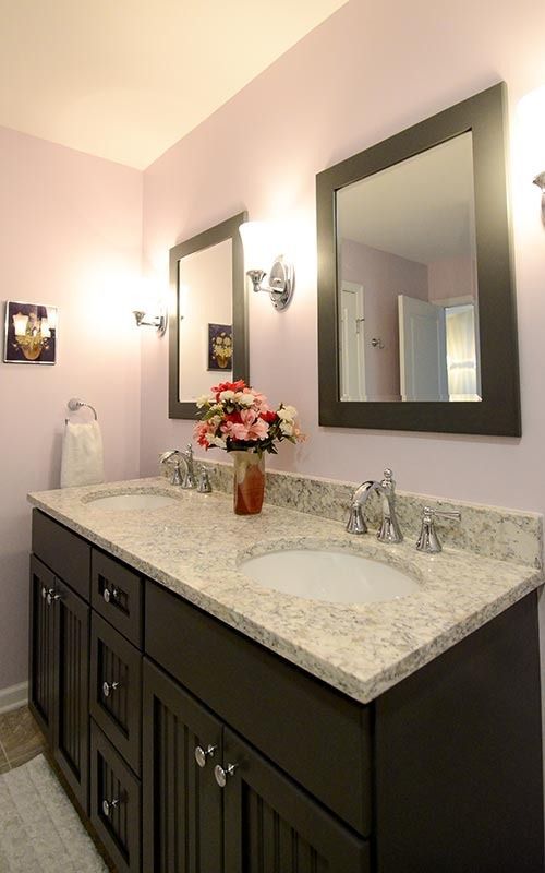 A dual-sink bathroom vanity with dark wood cabinets, a speckled granite countertop, and two framed mirrors on a pink wall.