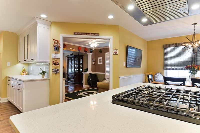 A modern kitchen with white cabinets and a quartz island featuring a gas stovetop, looking into a yellow-walled dining room.