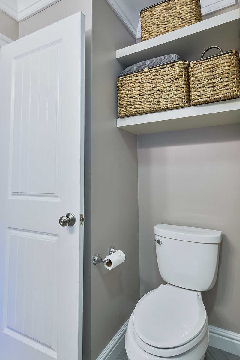 A toilet sits next to a white door in a bathroom with two floating shelves holding wicker baskets.