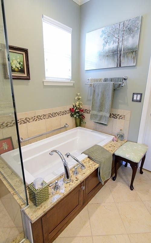 A bathroom featuring a white soaking tub with a beige stone surround, wooden cabinetry, and a green towel hanging nearby.
