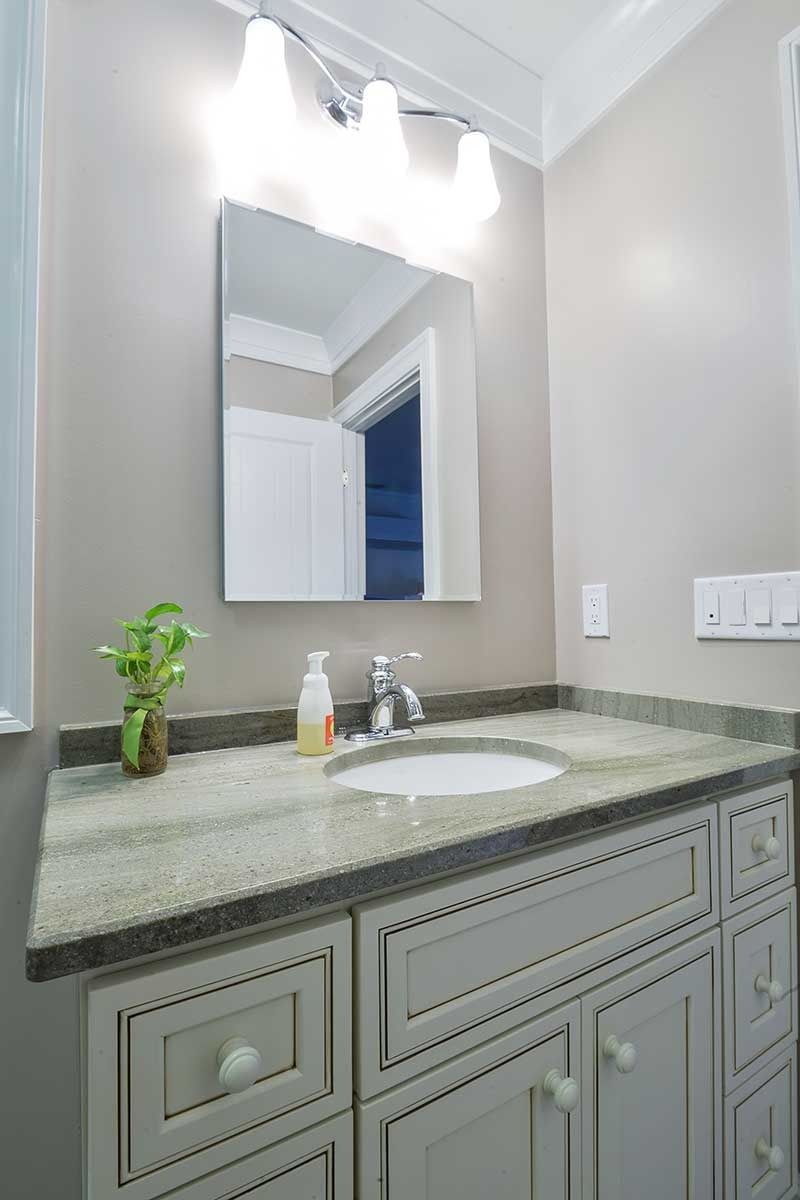 A bathroom vanity with a light gray cabinet, speckled granite countertop, square mirror, and three-light fixture above.