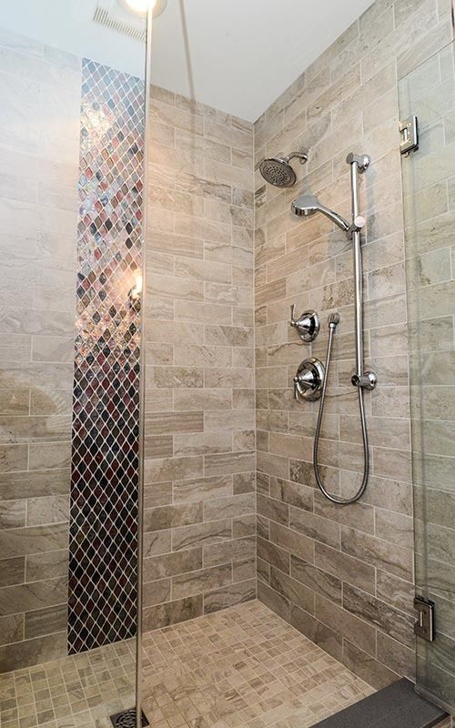 A walk-in shower with neutral stone tiles, a vertical decorative mosaic accent strip, and a chrome rainfall shower head.