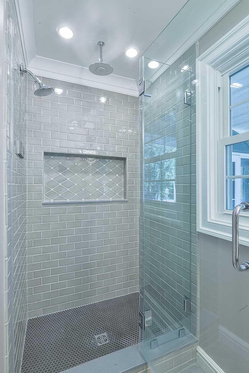 A modern glass-enclosed shower with gray subway tile walls, a recessed shelf, a ceiling rain showerhead, and a window.