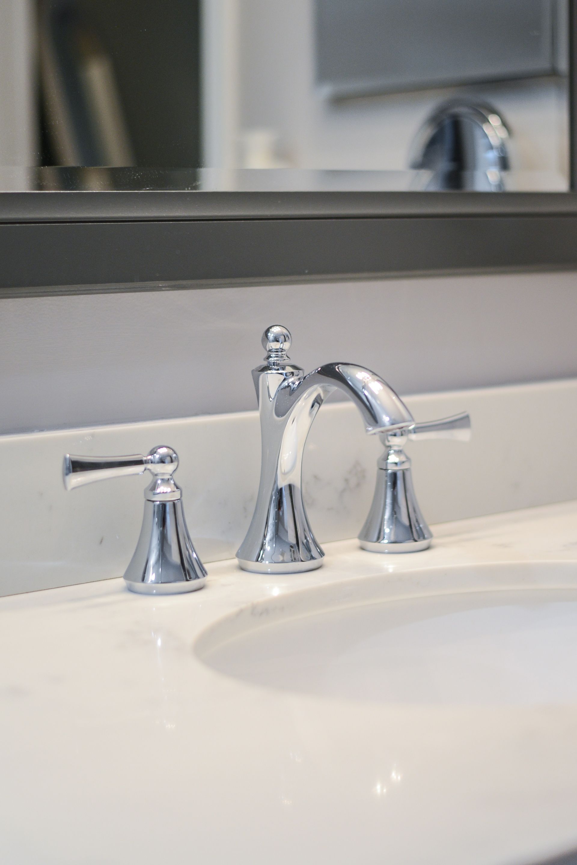 A chrome bathroom faucet set with two lever handles mounted on a white marble countertop.