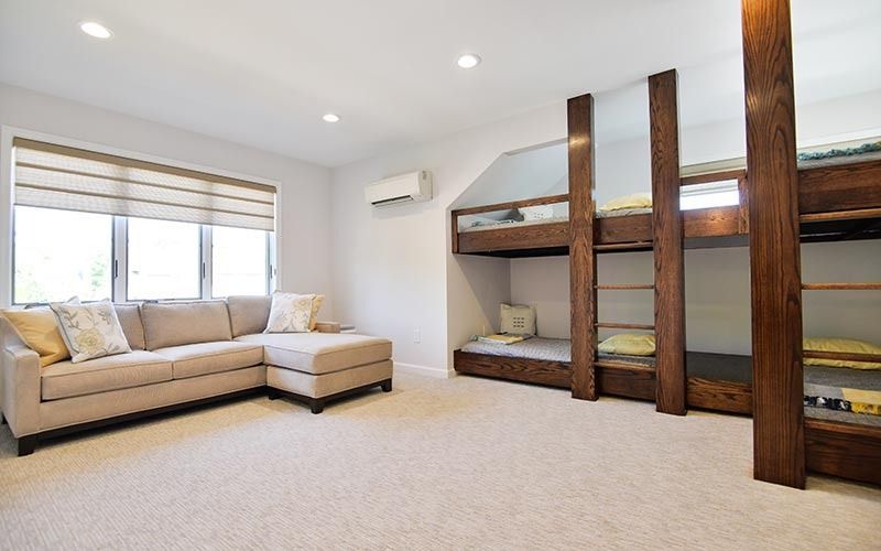 A beige sectional sofa sits in a room with light carpet, near a built-in wooden bunk bed structure against the wall.