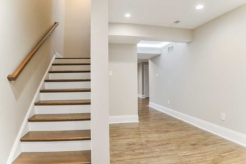 A wooden staircase with a simple handrail next to an open hallway with neutral walls and light wood-look flooring.