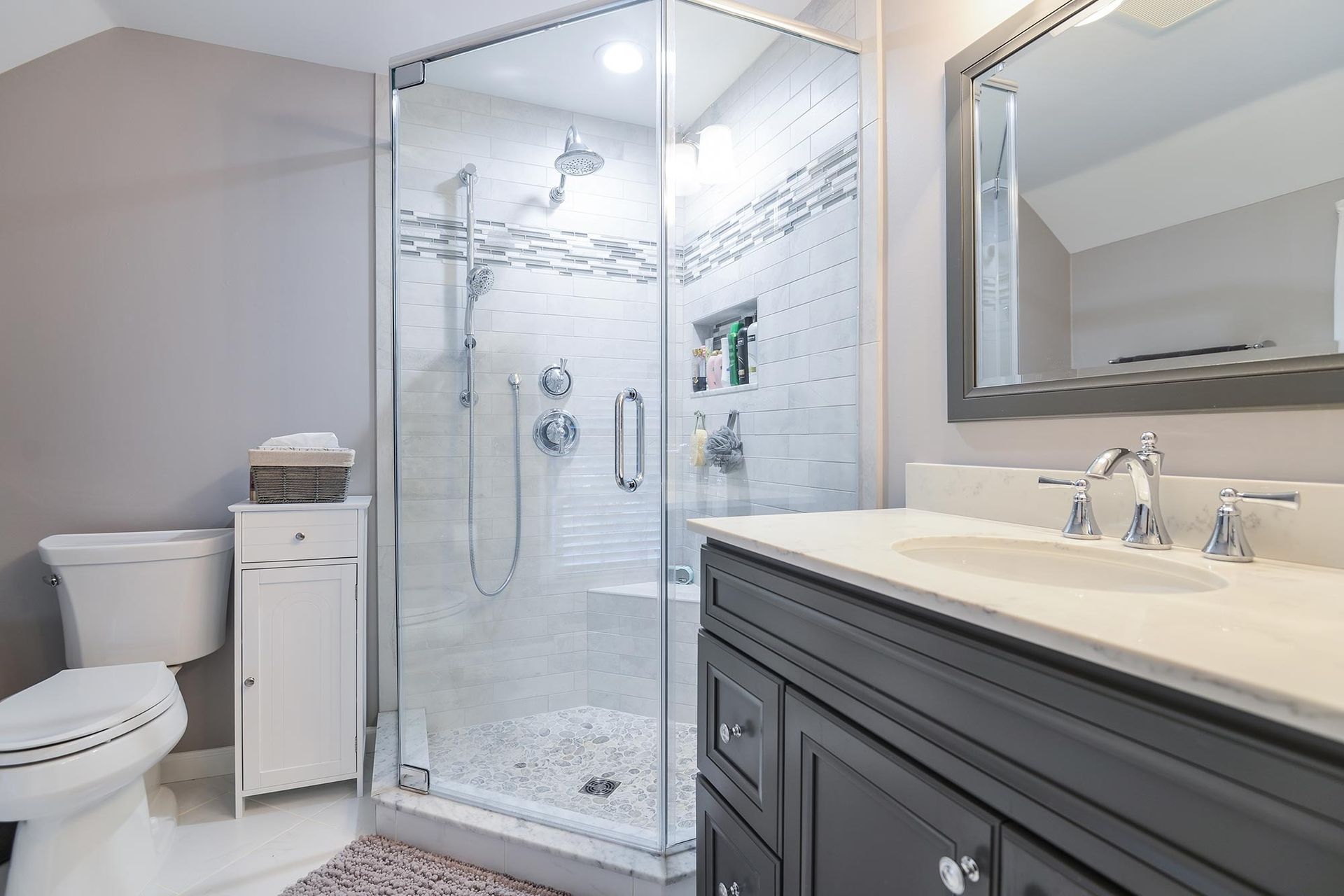 A modern bathroom with a glass-enclosed shower, a dark gray vanity with a cream countertop, and a white toilet.