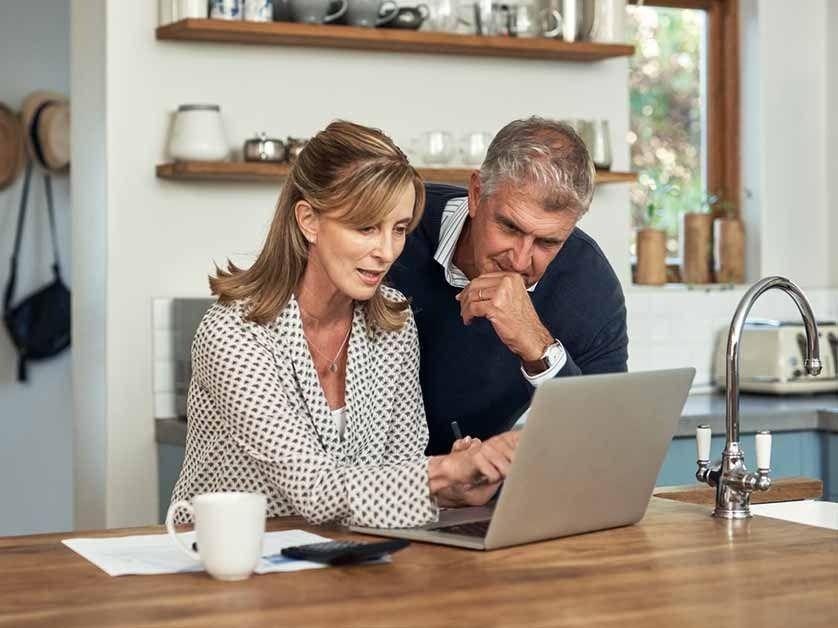 Two people in a kitchen looking at a laptop together, one pointing at the screen while the other looks on thoughtfully.