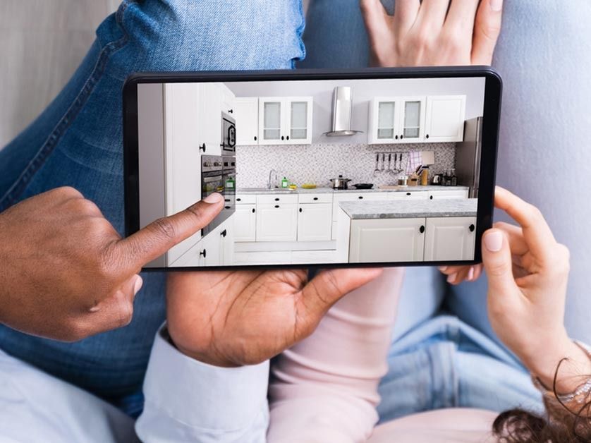 Two people look at a tablet screen displaying a photo of a modern white kitchen.