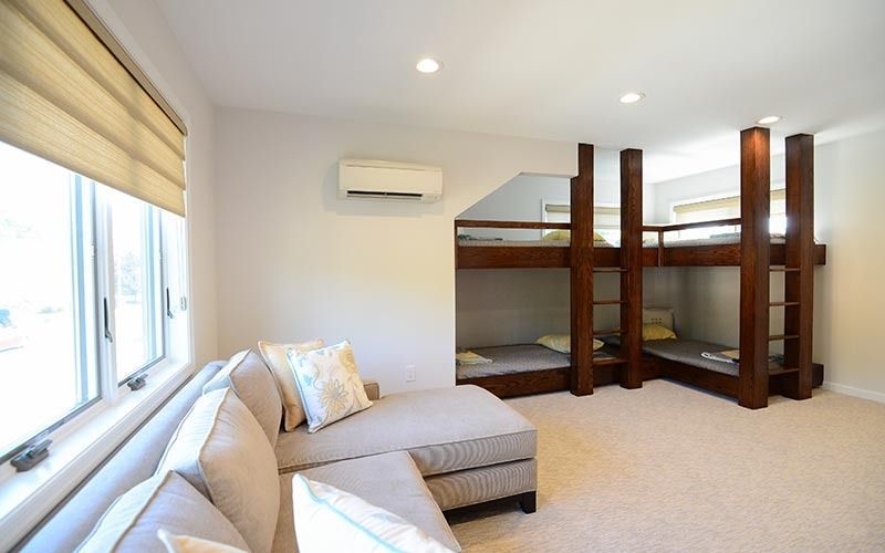 A cozy room with a grey sectional sofa, white walls, a window with tan shades, and a built-in wooden bunk bed structure.