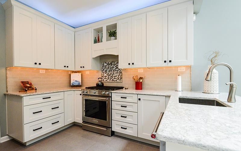 A bright, modern kitchen featuring white shaker cabinets, a stainless steel stove, and white marbled countertops.