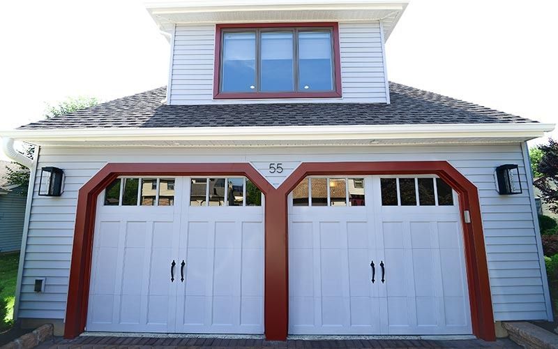 Detached garage with two white carriage-style doors, red trim, and a small loft window above.