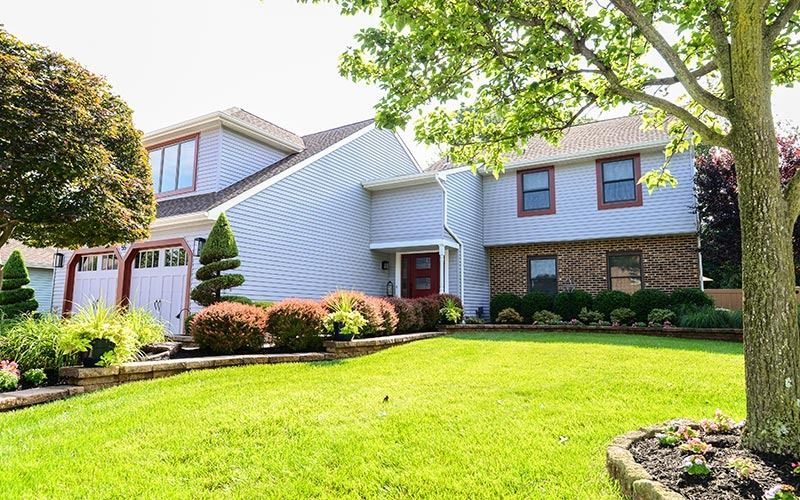 Two-story house with blue horizontal siding, a brick lower level, a front-facing garage, and a manicured lawn.