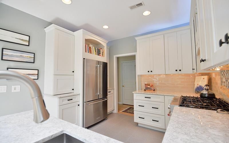 A modern kitchen with white cabinets, light gray walls, marble countertops, stainless steel fridge, and a gas stove.