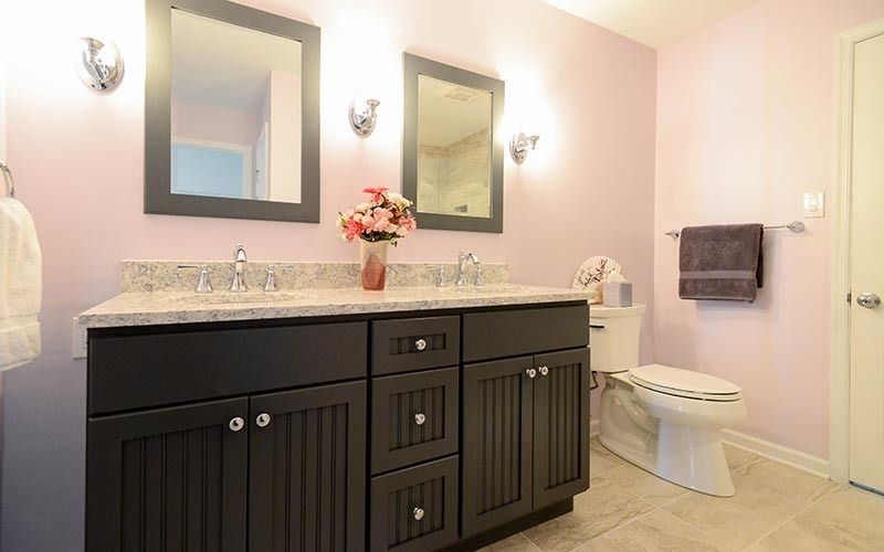 A bathroom with a dark-toned vanity, dual mirrors, light pink walls, and a white toilet against a neutral tile floor.