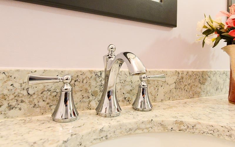 A shiny chrome three-piece bathroom faucet set mounted on a speckled, light-colored granite countertop.