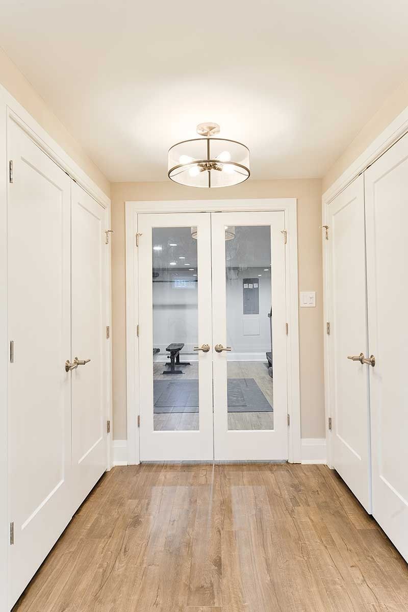 A hallway with white doors on both sides leads to French glass doors, featuring wood-look floors and a round ceiling light.