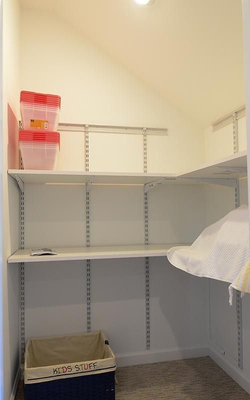 A small closet with white walls, two open shelves, and a storage basket on the floor labeled 