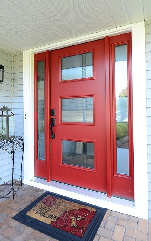A vibrant red front door with three horizontal rectangular glass windows, flanked by two side lights on a covered porch.