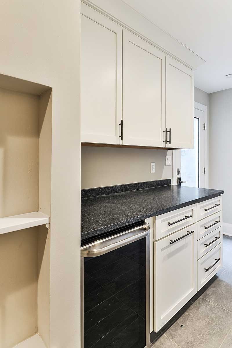 A kitchen area with white cabinets, a dark speckled countertop, a built-in wine cooler, and drawers next to a wall niche.