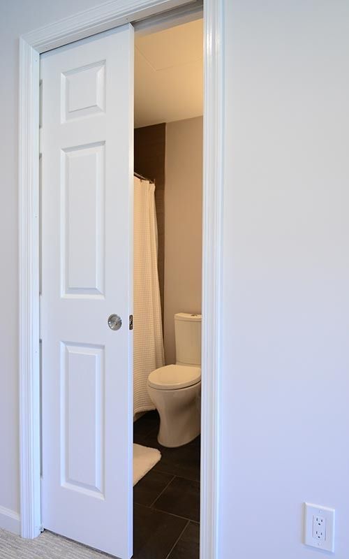 A white pocket door partially open to reveal a bathroom with a white toilet and shower curtain on a dark tiled floor.