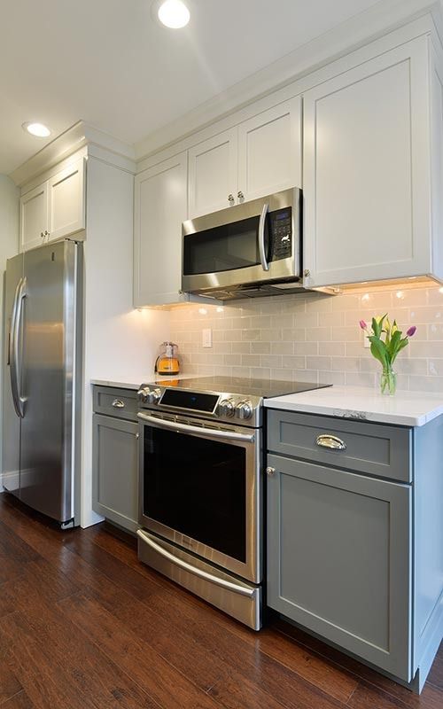 A modern kitchen featuring a stainless steel range and microwave, grey lower cabinets, white upper cabinets, and wood floors.