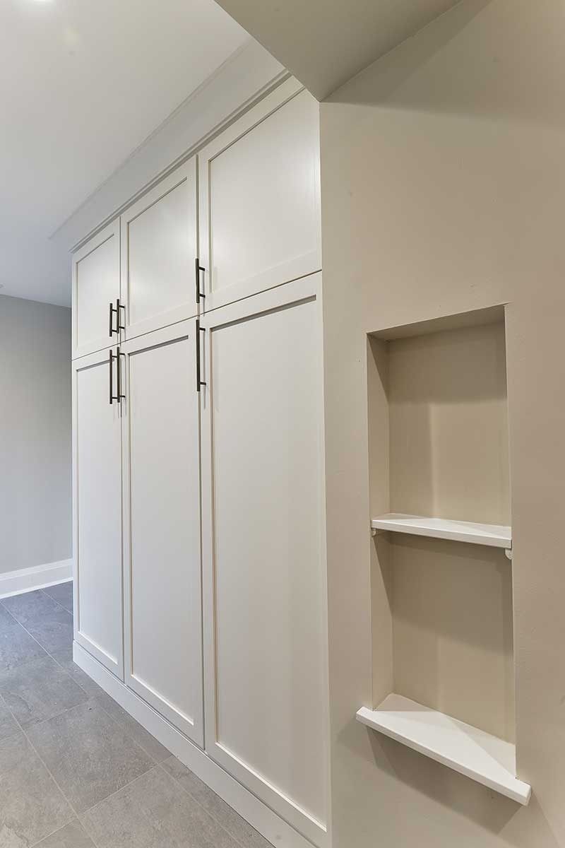 Built-in white floor-to-ceiling cabinets with dark handles next to a small recessed wall niche with two shelves.