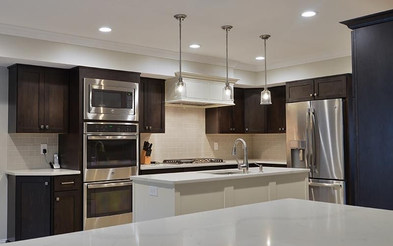 Modern kitchen featuring dark wood cabinets, stainless steel appliances, a white island with a sink, and pendant lighting.