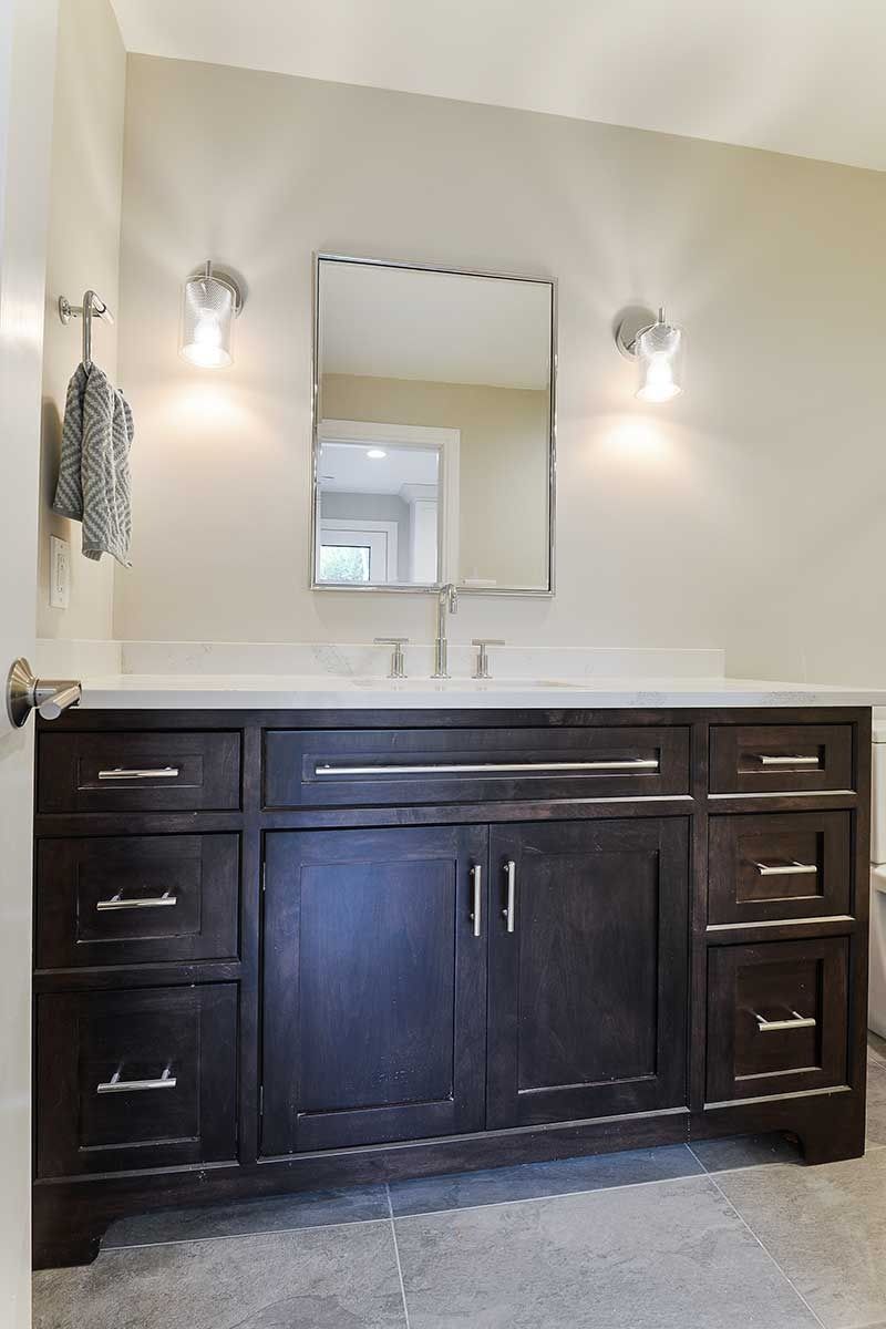 A bathroom vanity with a dark wood cabinet, white countertop, rectangular mirror, and two wall-mounted light fixtures.