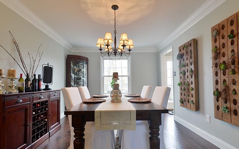 A dining room with a dark wood table, white chairs, a chandelier, and two vertical wall-mounted succulent planters.